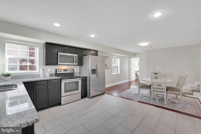 kitchen featuring baseboards, light stone counters, recessed lighting, appliances with stainless steel finishes, and a sink