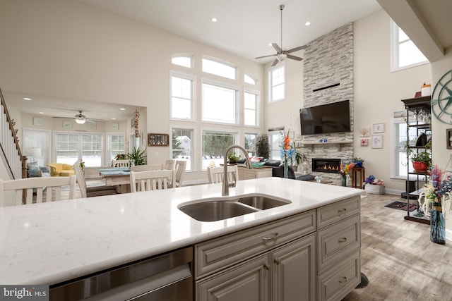 kitchen with a towering ceiling, sink, plenty of natural light, a stone fireplace, and light stone counters