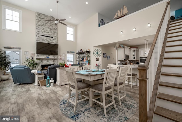 dining space with light hardwood / wood-style floors, plenty of natural light, a stone fireplace, and a towering ceiling