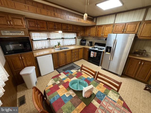 kitchen with white dishwasher, sink, wall oven, stainless steel fridge, and gas range