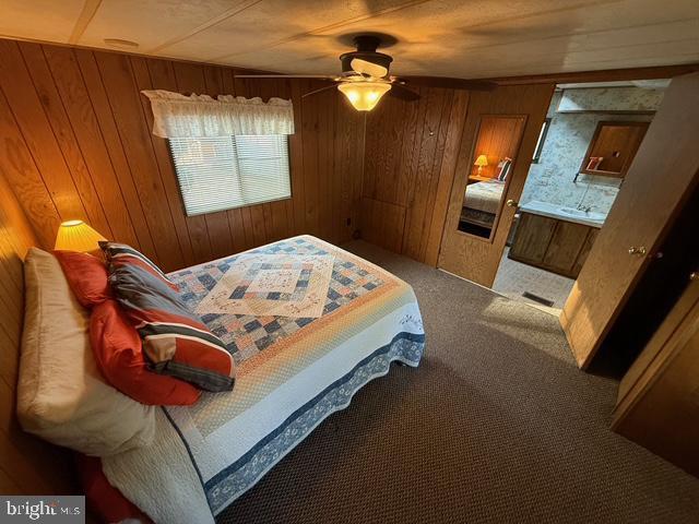 carpeted bedroom featuring wood walls and ceiling fan