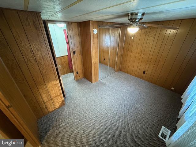 basement featuring ceiling fan, light colored carpet, and wood walls