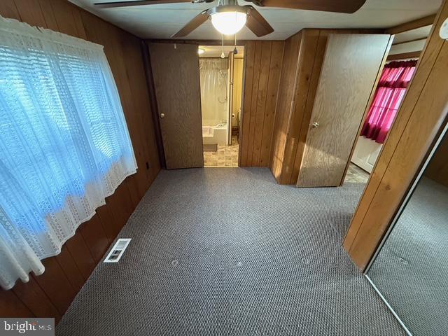 unfurnished bedroom featuring carpet flooring, wooden walls, a closet, and ceiling fan