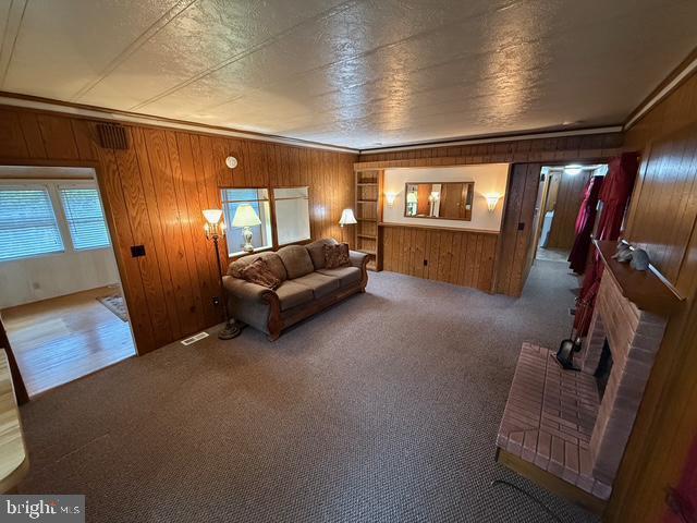 carpeted living room with crown molding, wooden walls, and a brick fireplace