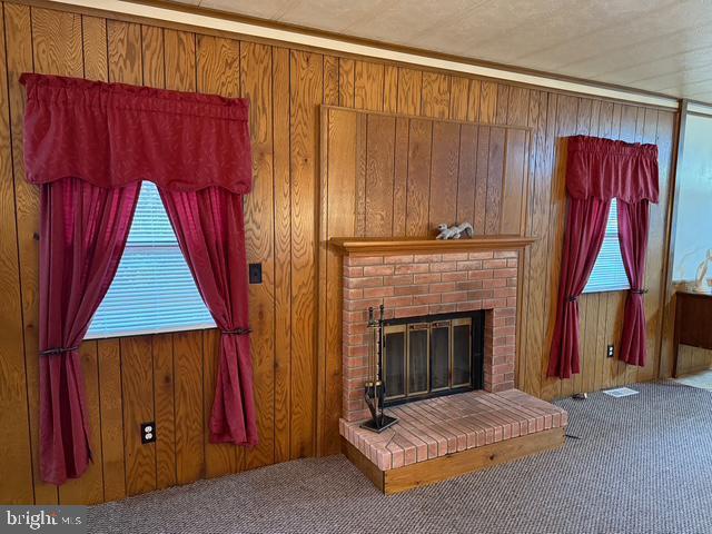 living room with a brick fireplace, carpet, and wooden walls