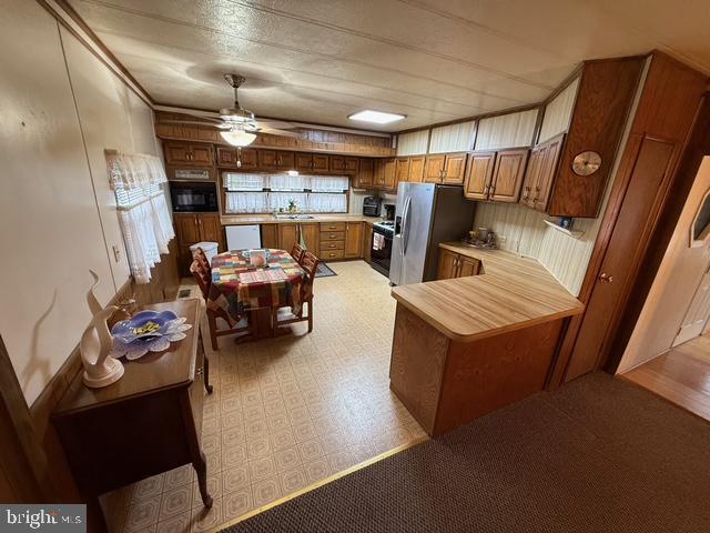 kitchen featuring range, stainless steel refrigerator with ice dispenser, black microwave, kitchen peninsula, and ceiling fan