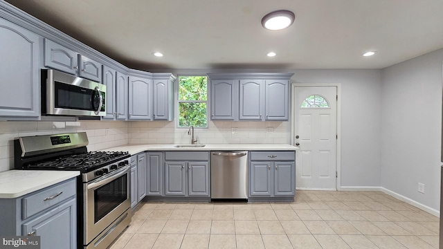 kitchen featuring stainless steel appliances, sink, backsplash, light tile patterned floors, and gray cabinetry