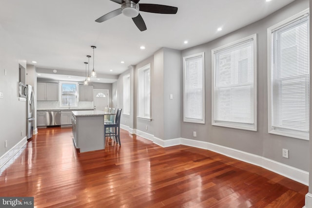 kitchen with a center island, decorative backsplash, gray cabinetry, decorative light fixtures, and stainless steel appliances