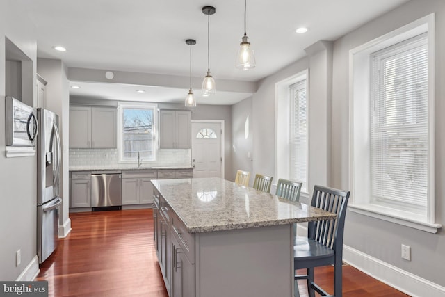 kitchen featuring appliances with stainless steel finishes, a center island, decorative light fixtures, backsplash, and a breakfast bar area