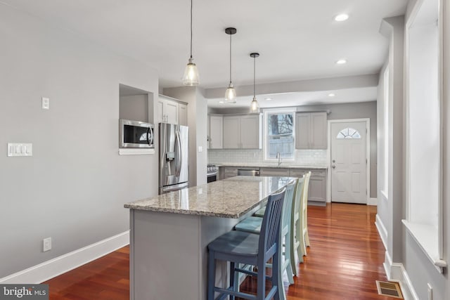 kitchen featuring a kitchen bar, appliances with stainless steel finishes, hanging light fixtures, a kitchen island, and backsplash