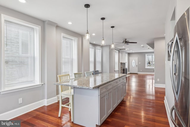 kitchen with stainless steel fridge, a kitchen breakfast bar, a kitchen island, pendant lighting, and gray cabinets