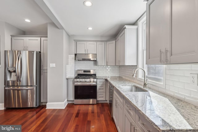 kitchen with appliances with stainless steel finishes, dark hardwood / wood-style flooring, tasteful backsplash, sink, and light stone counters