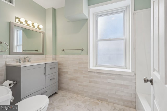 bathroom featuring vanity, toilet, tile walls, and a washtub