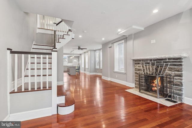 living room featuring ceiling fan, a stone fireplace, and wood-type flooring