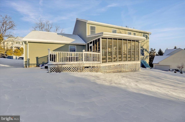 snow covered rear of property with a wooden deck and a sunroom