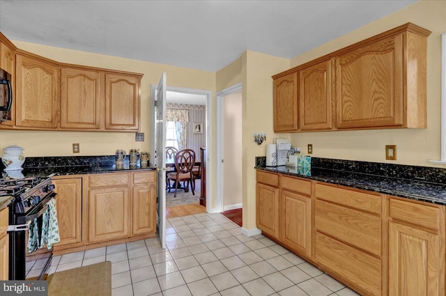 kitchen with dark stone countertops, black appliances, and light tile patterned flooring