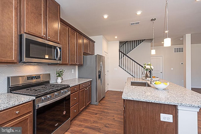 kitchen with sink, stainless steel appliances, light stone countertops, an island with sink, and decorative backsplash