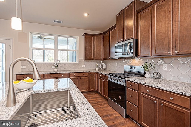 kitchen with light stone countertops, decorative light fixtures, stainless steel appliances, and backsplash