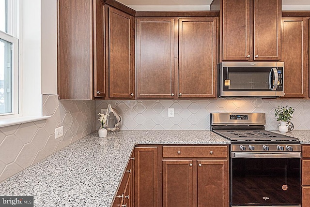 kitchen featuring appliances with stainless steel finishes, light stone countertops, and backsplash