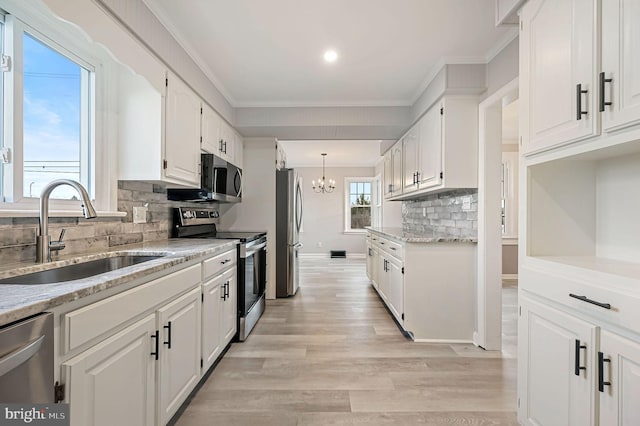 kitchen with sink, white cabinetry, stainless steel appliances, ornamental molding, and a chandelier