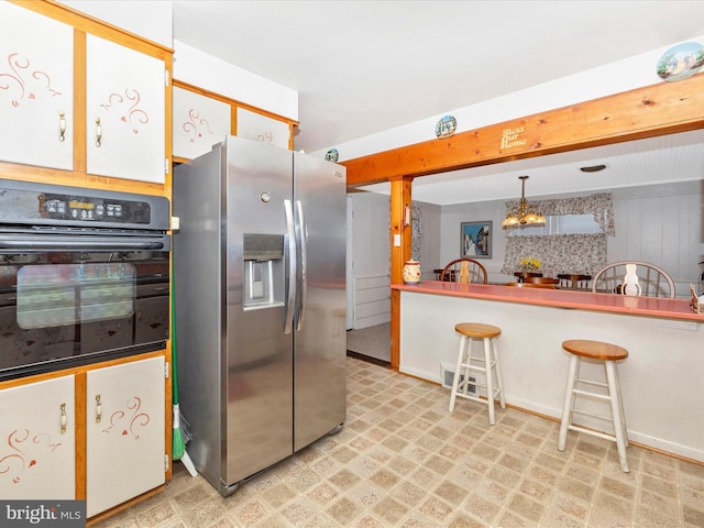 kitchen with stainless steel refrigerator with ice dispenser, a kitchen bar, white cabinetry, hanging light fixtures, and oven