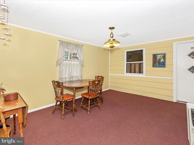 carpeted dining room featuring ornamental molding and wood walls