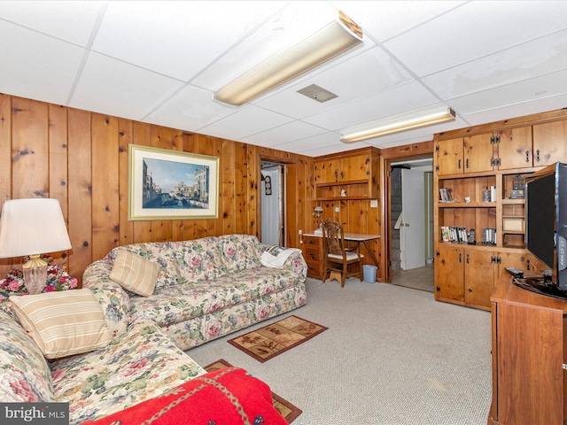 living room with light colored carpet, a drop ceiling, and wood walls