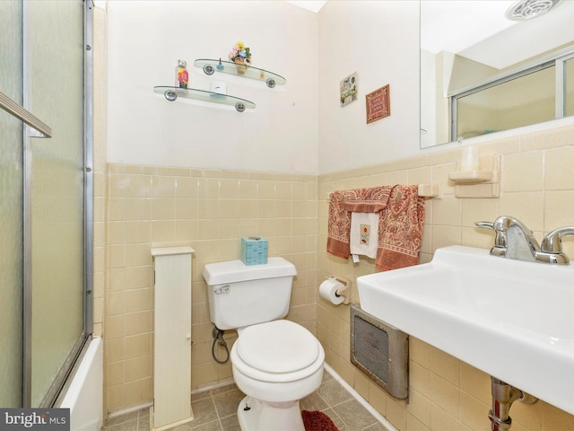 full bathroom featuring sink, combined bath / shower with glass door, tile patterned flooring, tile walls, and toilet