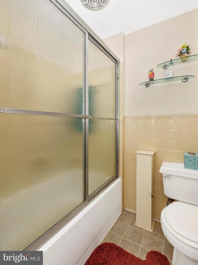 bathroom featuring tile walls, bath / shower combo with glass door, tile patterned floors, and toilet