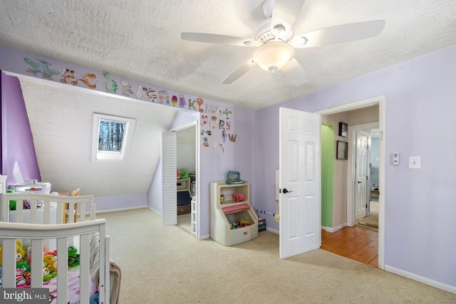 bedroom featuring a textured ceiling, ceiling fan, light colored carpet, and a crib