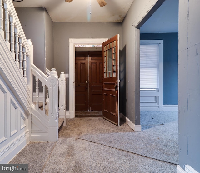 carpeted foyer with stairs, a ceiling fan, and baseboards