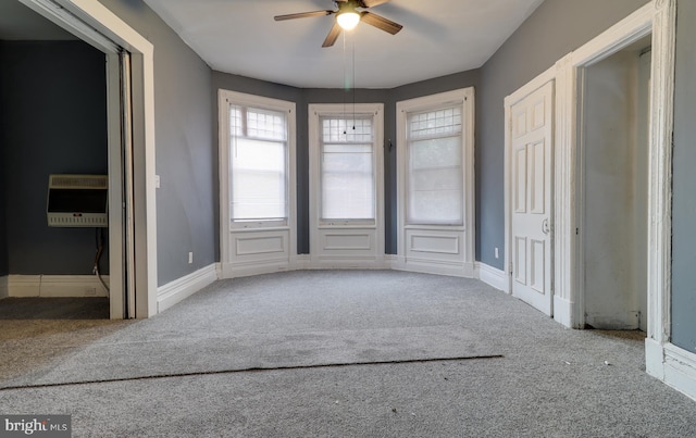 carpeted empty room with heating unit, baseboards, and ceiling fan