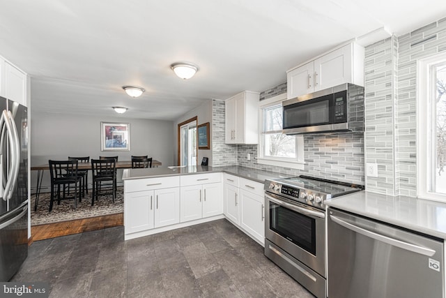 kitchen featuring white cabinetry, decorative backsplash, kitchen peninsula, and appliances with stainless steel finishes