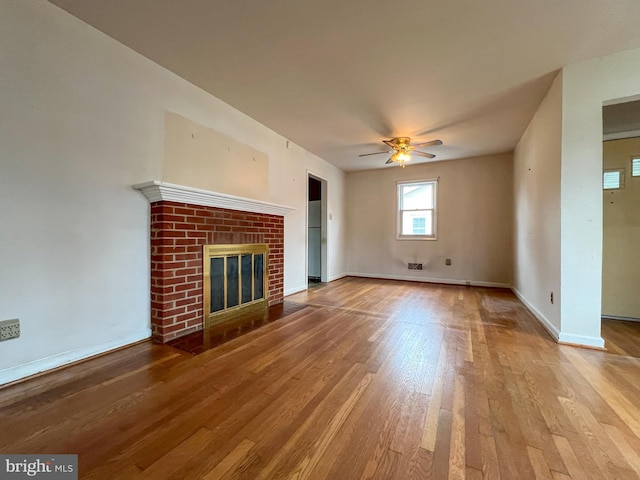 unfurnished living room featuring ceiling fan, a brick fireplace, and light hardwood / wood-style floors