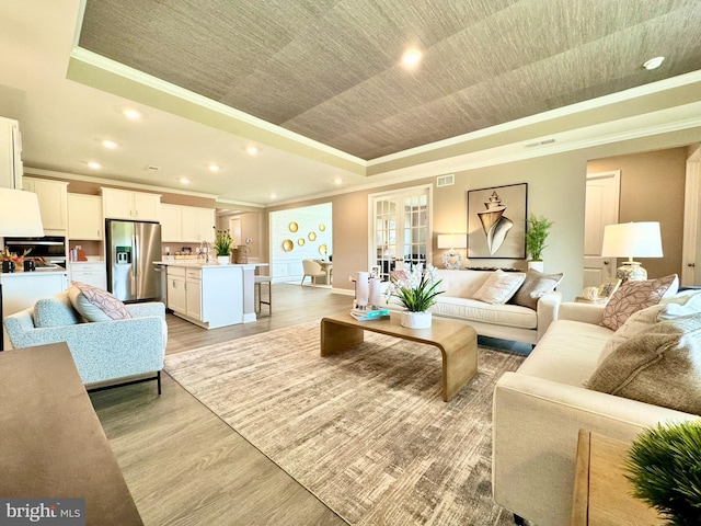 living room featuring a tray ceiling, crown molding, and light wood-type flooring