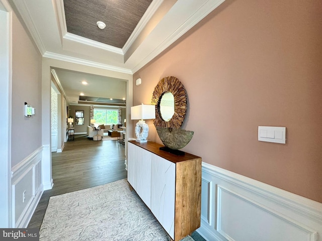 corridor with a raised ceiling, crown molding, and hardwood / wood-style flooring