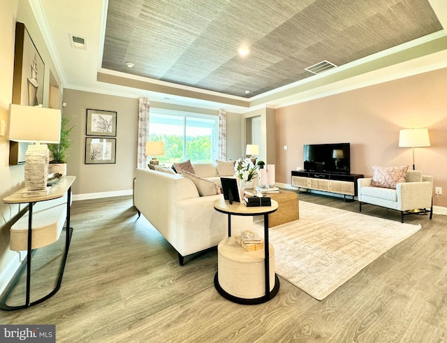 living room with hardwood / wood-style floors, ornamental molding, and a raised ceiling