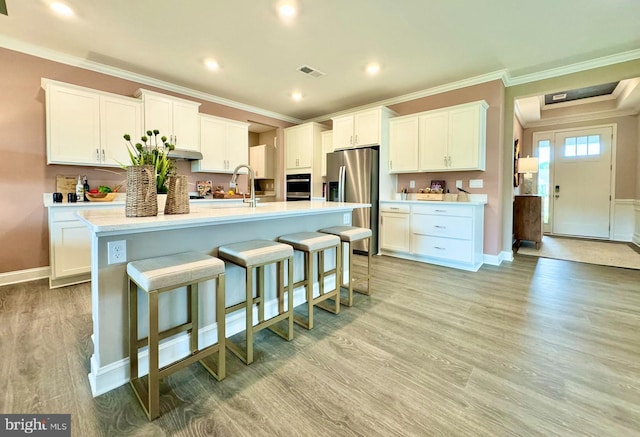 kitchen with white cabinets, an island with sink, stainless steel fridge, light hardwood / wood-style flooring, and a breakfast bar area