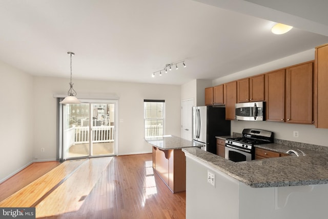 kitchen featuring stainless steel appliances, hanging light fixtures, light wood-style floors, brown cabinetry, and a kitchen breakfast bar