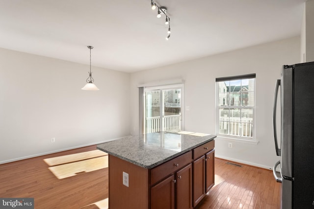 kitchen featuring brown cabinetry, a center island, decorative light fixtures, freestanding refrigerator, and stone counters