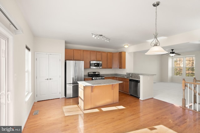 kitchen with a breakfast bar area, hanging light fixtures, appliances with stainless steel finishes, open floor plan, and light wood-type flooring