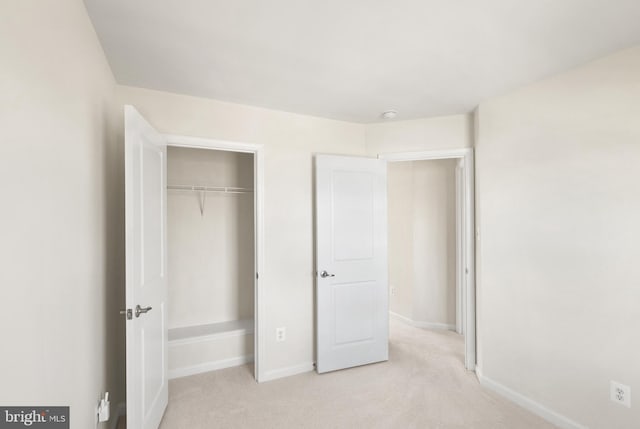 unfurnished bedroom with a closet, light colored carpet, and baseboards