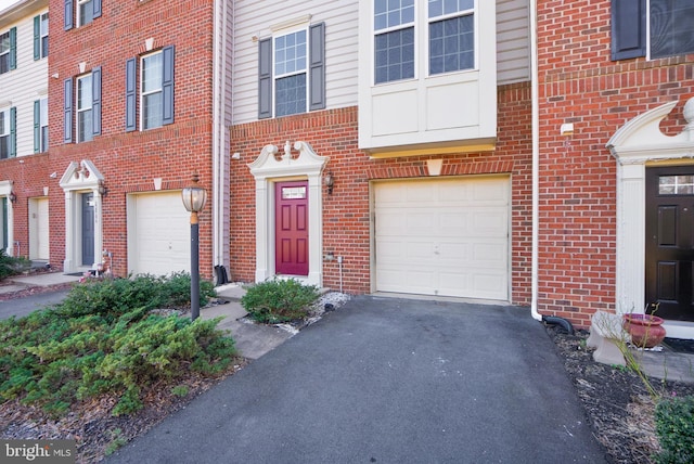 property entrance featuring a garage, aphalt driveway, and brick siding