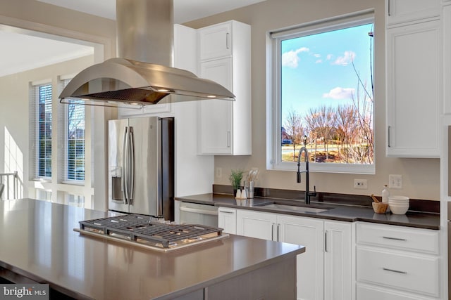 kitchen with dark countertops, appliances with stainless steel finishes, white cabinets, a sink, and island range hood