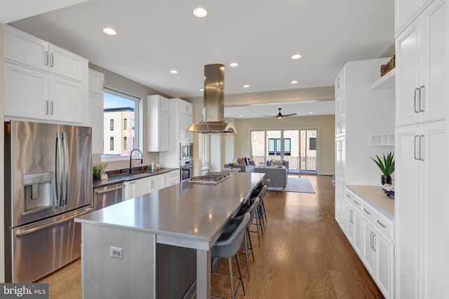 kitchen featuring white cabinets, a kitchen island, appliances with stainless steel finishes, open floor plan, and island exhaust hood