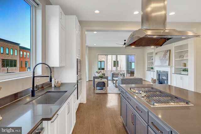 kitchen featuring island range hood, a sink, white cabinetry, open floor plan, and dark countertops