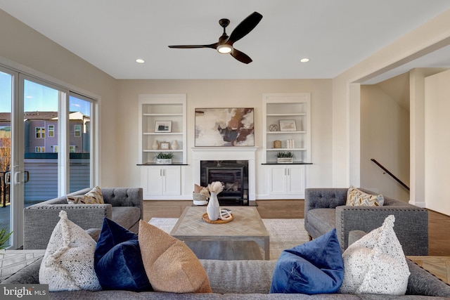 living area with built in features, a glass covered fireplace, recessed lighting, and wood finished floors