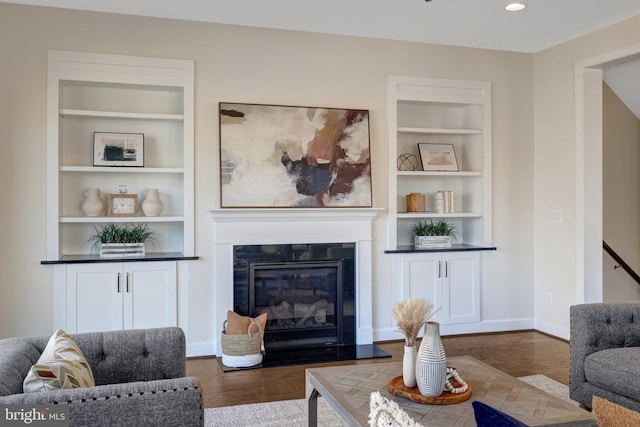 living room featuring built in shelves, recessed lighting, baseboards, dark wood-style floors, and a glass covered fireplace