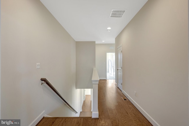 hall featuring baseboards, visible vents, wood finished floors, and an upstairs landing