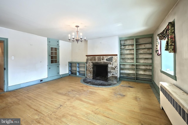 unfurnished living room featuring an inviting chandelier, radiator heating unit, a fireplace, built in shelves, and light wood-type flooring